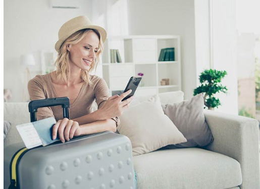 Woman with hat leaning on luggage and looking at smartphone