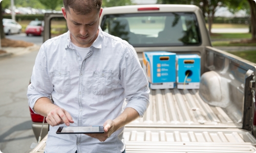 Dealer leaning over back of truck holding smart phone and OvrC logo at the top of image