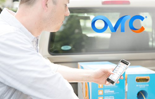 Dealer leaning over back of truck holding smart phone and OvrC logo at the top of image