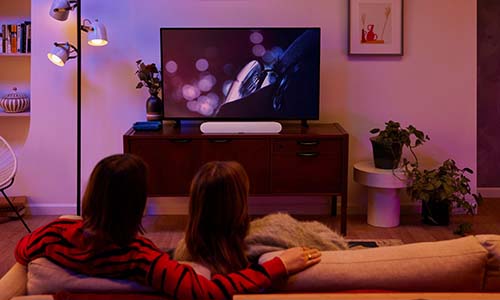 White Sonos Ray soundbar on an entertainment center with couple watching TV