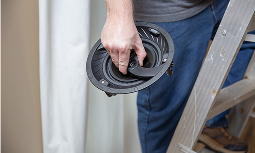 Installer holding speaker during install while standing on a ladder