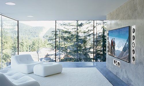 Sleek , windowed living room with white couch and flat screen and speakers mounted in wall