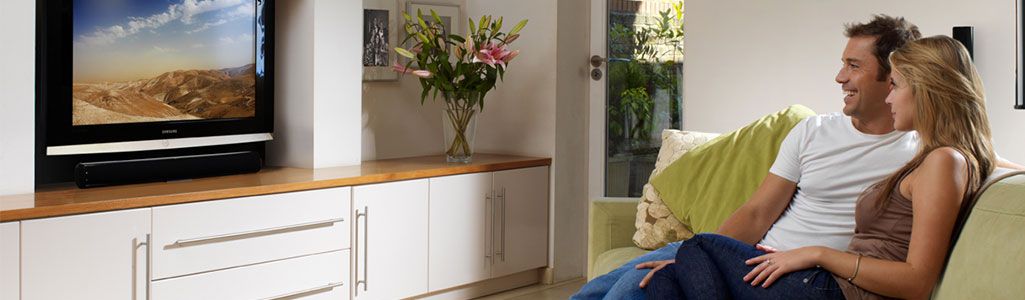 Man and woman lounging on couch while watch TV with soundbar below it