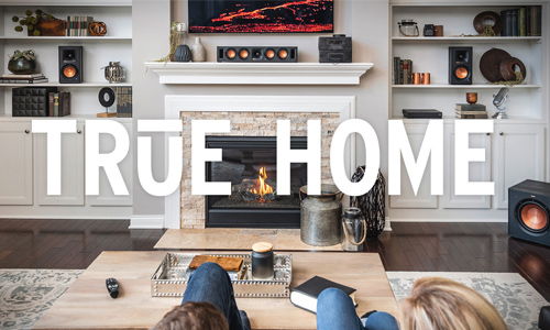 Living room scene with Klipsch products setting on built-in shelves and the subwoofer in the corner on the floor and True Home text overlayed on image