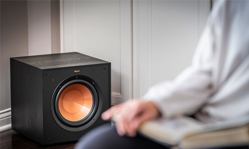 Cropped image of blurred person sitting in a chair and the subwoofer in focus in the corner of room 