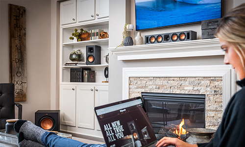 Woman using laptop with Klipsch products on mantle and built-in shelves behind her