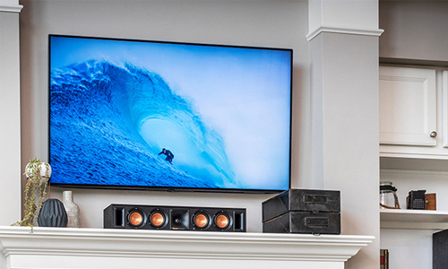 Center channel speaker setting on fireplace mantle below flat screen TV