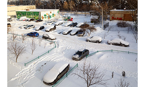 Several cars in parking lot with snow on top on them