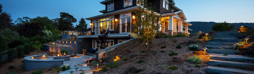 House with landscape lighting on patio and stairs leading up to house