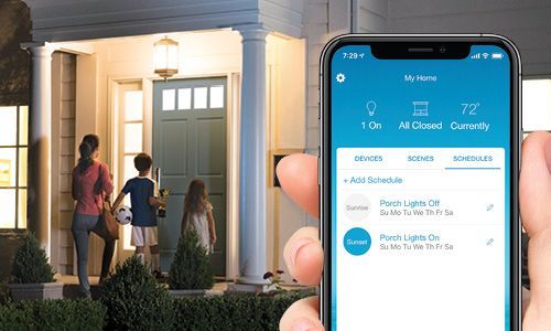 Hand holding smartphone showing Lutron app in foreground and family standing at front door in background
